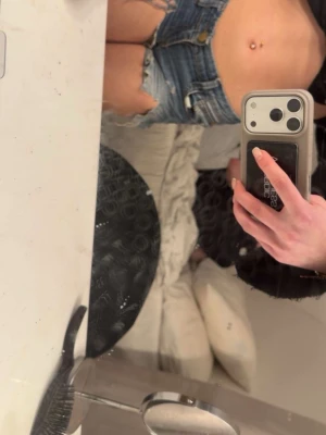 Blå jeansshorts lågmidjade med fransig kant - Säljer ett par klassiska blå jeansshorts med rå, fransig kant och slitna detaljer. Shortsen har fem fickor, bälteshällor och knappgylf. Perfekta för varma dagar och en avslappnad look.