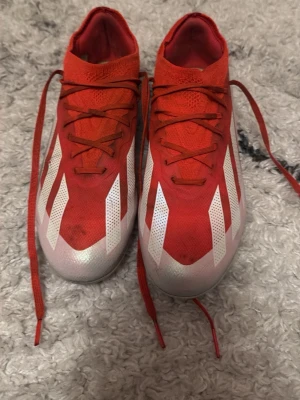 Röda Adidas fotbollsskor med vita ränder  - Säljer ett par snygga röda Adidas fotbollsskor med klassiska vita ränder på sidorna. Skorna har låg profil, snörning och ovandel i syntetmaterial för bra bollkontroll. Perfekta för dig som vill sticka ut på planen! Finns att hämta i Gävle ingen posnord enast face mot face i gävle kan mätas upp Storlek 38
