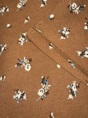 Brun blommig kjol med dragkedja - Säljer en brun kortkjol med små vita och blå blommor. Kjolen har en diskret dragkedja i sidan och är lätt utsvängd för en snygg outfit. Pris kan diskuteras