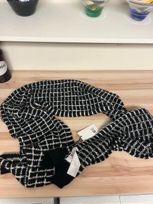 Svartvit stickad halsduk från CC - Säljer en svartvit stickad halsduk från CC med rutigt mönster. Halsduken är mjuk och har en skön struktur, perfekt för kyliga dagar. Aldrig använd!