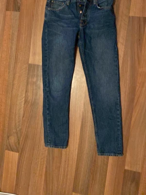 Mörkblå raka jeans - Säljer ett par mörkblå jeans med rak passform och klassisk femficksdesign. Jeansen har hög midja, knappgylf och detaljerade sömmar på bakfickorna. Tillverkade i denim, perfekta för en avslappnad och stilren look. Kan gå ner lite i pris då det inte är fast, jag är lite flexibel då jag bara vill bli av med dessa jeans då jag aldrig använt dem o de tar bara plats i garderoben 