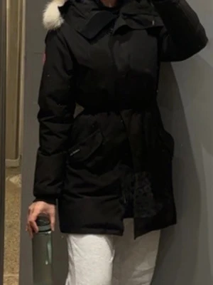 Canada Goose Rosclair parka  - Säljer en svart parkas från Canada Goose med klassisk patch på ärmen och stora fickor framtill. Jackan har lång ärm, hög krage och dragkedja. Dessutom kan man justera vid midjan innanför jackan 