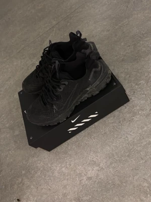 Svarta Nike sneakers med meshdetaljer - Säljer ett par helsvarta Nike sneakers med cool meshdesign och robust sula. Skorna har klassisk snörning och diskret swoosh på sidan. Perfekta för dig som gillar sportig och stilren look. Levereras i originalkartong. Köptes nyss kan tvättas blir rena som ny.