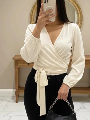 Vit omlottopp med knytband - Snygg vit omlottopp med långa ärmar och breda knytband i midjan. Toppen har v-ringning och är croppad, vilket ger en trendig look. Perfekt att styla med höga jeans eller kjol för en chic outfit.