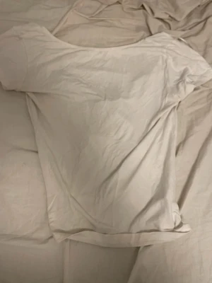 Vit topp med rosett och kort ärm - Söt vit topp med korta ärmar och en stor, glansig rosett framtill. Toppen har en enkel, rund halsringning och är gjord i ett mjukt material som känns skönt mot huden. Perfekt för dig som gillar en feminin och stilren look.