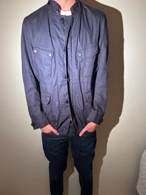 Woolrich jacka  - Stilren och funktionell Woolrich jacka i mörkblå ton. Klassisk design med flera fickor och en modern passform – perfekt som vardagsjacka vår/höst. ✔️Märke: Woolrich✔️ Storlek: L✔️ Passform: Normal–slim✔️ Färg: Mörkblå ✔️ Skick: Mycket bra begagnat skick✔️ Stil: Field jacket / casual ✔️ Funktioner: Flera fickor, dragkedja + knäppning  Jackan sitter snyggt på kroppen (se bild). Inga hål, fläckar eller trasiga sömmar. 