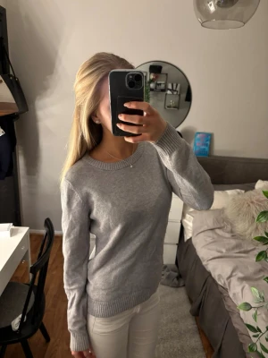 Ljusgrå stickad tröja i basic stil - En enkel och stilren ljusgrå stickad tröja med rund halsringning och ribbade muddar vid ärmslut och nederkant. Perfekt för lager-på-lager och passar till det mesta. Tröjan har en klassisk passform och är gjord i mjukt material.