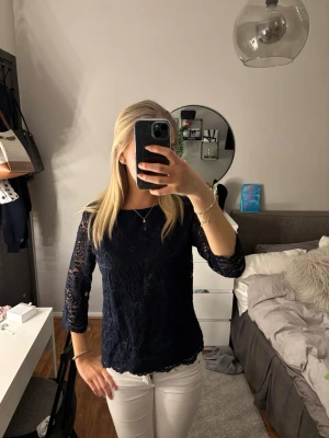 Mörkblå spetsblus med trekvartsärm - Snygg mörkblå blus i spets med trekvartsärmar och rund hals. Blusen har en feminin och elegant look med transparenta ärmar och lätt figurnära passform. Perfekt att styla med både jeans och kjol.