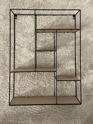 Vägghylla i trä och metall - Snygg vägghylla med flera hyllplan i ljust trä och svart metallram. Hyllan har en modern, geometrisk design med olika stora fack. (Säljs inte längre) ordinarie pris 770kr säljer för 199kr 