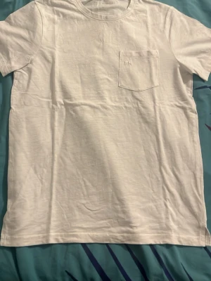 Vit t-shirt med bröstficka och RM-logga - Klassisk vit t-shirt med rund hals och korta ärmar. På bröstet finns en liten ficka med diskret RM-Race Marine logga broderad. Tillverkad i mjuk bomull som känns skön mot huden. Perfekt basplagg för alla tillfällen. Scandinavian märke!