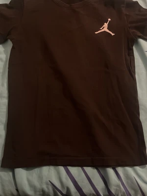 Brun Jordan t-shirt med logga - Snygg brun t-shirt från Jordan med den klassiska Jumpman-loggan i vitt på bröstet. T-shirten har korta ärmar och är gjord i mjuk bomull för skön känsla. Perfekt för dig som gillar streetwear och sportig stil.Den är helt okej faktist väldigt bra på gymmet och logon är helt okej men man ser lite saker.