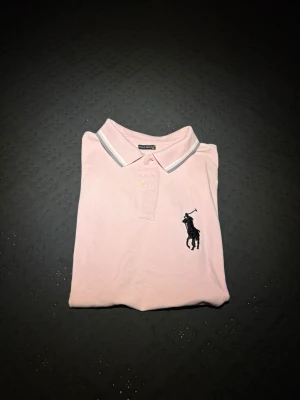 Rosa pikétröja från Ralph Lauren - Klassisk ljusrosa pikétröja från Ralph Lauren i storlek 3XL men sitter betydligt mycket mindre, skulle vilja säga XL. (Fråga om mått i PM). Annars en jättesnygg piké som passar en laidback eller grisch stil