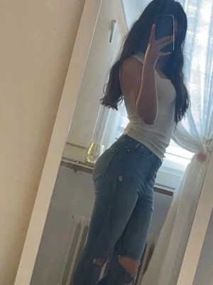 Blå slitna skinny jeans - Säljer ett par blå skinny jeans med slitningar vid knäna. Jeansen har hög midja och klassisk femficksdesign. Perfekta för en avslappnad och trendig look. Materialet är stretchigt denim som sitter snyggt och bekvämt.