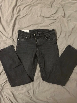 Svarta raka jeans från HM - Säljer ett par svarta jeans från HM med rak passform och klassisk femficksdesign. Jeansen har silverfärgade nitar och knapp, samt bälteshällor. Materialet är denim i bomull med en snygg tvättad look. Perfekta till en avslappnad stil.