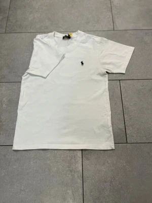Vit t-shirt från Ralph Lauren - Klassisk vit t-shirt från Ralph Lauren med liten broderad logga på bröstet. T-shirten har korta ärmar och v-ringad hals. Perfekt basplagg i mjuk bomull som passar till allt.