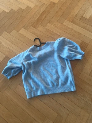 Ljusblå tröja med puffärm - Supersöt ljusblå tröja med trendiga puffärmar och ribbade muddar. Kortare modell som passar perfekt till både jeans och kjol. Mjuk och skön, troligtvis i bomull eller bomullsblandning. Enkel rund halsringning och stilren design.