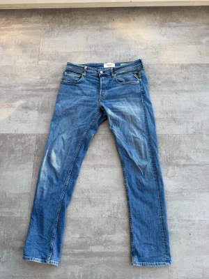Blå straight fit jeans från Replay - Säljer ett par blå jeans från Replay, modell Grover med straight fit. Jeansen har klassisk femficksdesign, knappgylf och snygga. Perfekta för dig som gillar en avslappnad och tidlös stil.