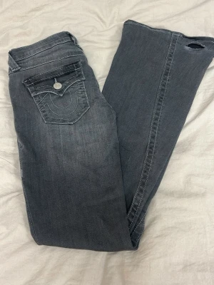 Grå Lågmidjade jeans från true religion - Grå jeans från true religion som inte längre kommer till användning! De har blivit slitna längst ner då de varit för långa för mig, se bilder. Annars är du i superfint skick! Pris kan diskuteras!!