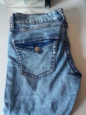 Ljusblå jeans med lila detaljer  - Säljer ett par ljusblå jeans med bootcut  och unika bakfickor med ficklock och knappdetaljer. Jeansen har kontrastsömmar i lila och klassisk femficksdesign. Perfekta för en avslappnad och trendig look. Storlek 164, använda en gång . Pris kan diskuteras 