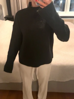 Svart stickad polotröja - Mysig svart stickad polotröja med lång ärm och avslappnad passform. Tröjan har ribbstickade muddar och hög krage som ger extra värme. Perfekt för kalla dagar och enkel att matcha med olika outfits.