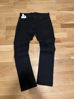 Svarta raka jeans från Ralph Lauren - Säljer ett par svarta jeans från Ralph Lauren med klassisk femficksmodell och raka ben. Jeansen har diskret logga på linningen och är tillverkade i ett mjukt denimtyg som sitter snyggt. Perfekta för dig som gillar stilrena och tidlösa plagg.