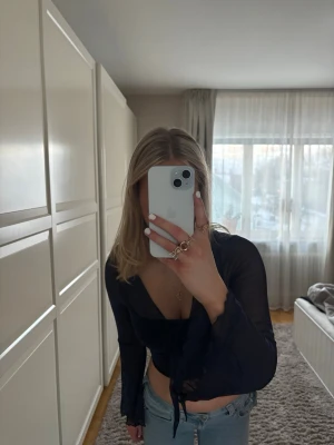 Svart mesh topp med knyt framtill - Trendig marinblå mesh topp med långa ärmar och snygg knytning framtill. Toppen är croppad och har en djup v-ringning som ger en modern look. Perfekt att styla med jeans eller kjol för en cool outfit.