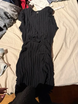 Svart kortklänning med struktur - Säljer en svart kortklänning med ribbad struktur och rund hals. Klänningen har korta ärmar och markerad midja för en snygg siluett. Perfekt för dig som gillar enkel men stilren design.