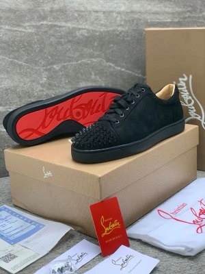 Svarta Christian Louboutin sneakers - Snygga svarta sneakers från Christian Louboutin med mattsvarta nitar på tån och klassisk röd sula. Skorna har lågt skaft, svarta skosnören och är tillverkade i mocka och läder. Perfekta för dig som vill sticka ut med en lyxig och edgy stil.