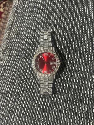 Röd glittrig klocka med stenar - Säljer en riktigt snygg klocka från Geneva med röd urtavla och datumvisning. Armbandet och boetten är täckta av glittrande stenar som ger en lyxig känsla. Klockan har en klassisk rund form och är i silverfärg. Perfekt för dig som vill sticka ut!