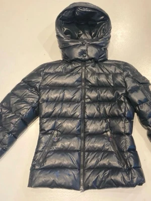 Svart dunjacka med huva - Fin varm jacka. Äkta moncler.  Bra skick, men med slitage på dragkedjehängena. Ett hänge har fallit av och ersatts med en svart pryl (se bild – påverkar inte dragkedjans funktion). Det finns en liten reva på insidan längst ner på dragkedjan (se bild). Storlek S, passar XS. Pris kan diskuteras 