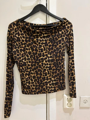 Leopardmönstrad långärmad topp - Snygg långärmad topp med leopardmönster i bruna och svarta toner. Toppen har en något bredare halsringning och är figurnära i modellen. Perfekt för dig som vill sticka ut med ett djuriskt print.