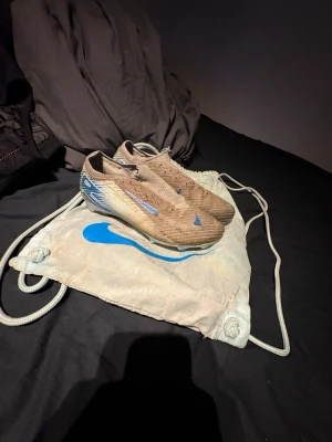 Nike Mercurial fotbollsskor blå/beige - Säljer ett par Nike Mercurial fotbollsskor i beige med blå detaljer och vit sula. Skorna har en strömlinjeformad design och är tillverkade i syntetmaterial för bästa grepp och känsla på planen. Perfekta för dig som vill ha snabbhet och kontroll. De är rätt skabbiga men det är elites och dem kostar 3000 nypris men de borde hålla någon månad till, kan även försöka tvätta dem men det gör jag om någon är bra intresserad 
