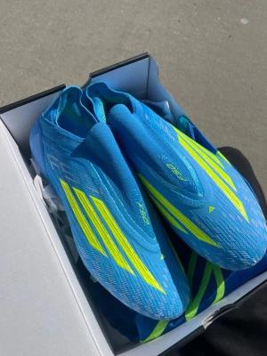 Adidas blåa f50 - Säljer ett par Adidas X Speedflow fotbollsskor i en snygg blå färg med gula detaljer och klassiska tre ränder. Skorna har en strömlinjeformad design och är tillverkade i lätt syntetmaterial för maximal fart på planen. Perfekta för dig som vill sticka ut och spela snabbt.