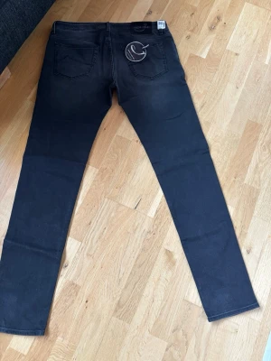 Svarta skinny jeans från Jack & Jones - Säljer ett par svarta skinny jeans från Jacob cohën med diskreta slitningar, aldrig använd bara prövad. Jeansen har en smal passform och stretchigt material som sitter tajt längs benen. Perfekta för en trendig och avslappnad stil. Innerbenslängd 90 cm, totalt längd 117 cm.