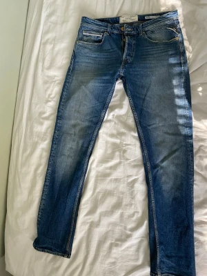 Blå jeans från Replay - Snygga blå jeans från Replay med klassisk femficksdesign och ljusa slitningar på framsidan. Jeansen har en läderpatch med logga bak och är tillverkade i denim med stretch för extra komfort. Modell replay Grover storlek W32 L32. Bra skick sparsamt använda. Nypris 1900 mitt pris 300