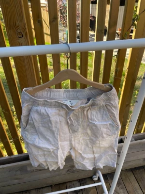 Beiga linneshorts med snörning - Säljer ett par beiga shorts i linne med avslappnad passform och snörning i midjan. Två sidofickor och en bakficka. Perfekta för varma dagar och enkel stil. Storlek på sista bild.