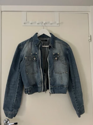 Unik jeansjacka  - Snygg blå jeansjacka med kortare passform och coola detaljer. Saknar några paljetter (se bilder). Storlek L men liten i storlek så skulle säga att den passar xs/s
