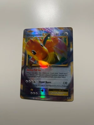 Dragonite EX Pokémonkort holo - Säljer ett Dragonite EX Pokémonkort med holografisk yta. Kortet har 180 HP och visar Dragonite i färgstarka nyanser av orange och gult. Text och detaljer i silver och blått. Perfekt för samlare eller Pokémonfans.