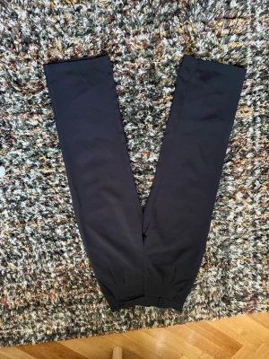 Svarta raka kostymbyxor - Säljer ett par svarta kostymbyxor med rak passform och klassisk design. Byxorna har pressveck och är tillverkade i ett slätt tyg som ger en stilren look. Perfekta för dig som vill ha en clean och enkel stil.