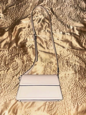 Beige/krämvit väska  - Stilren beige axelväska med justerbar rem 