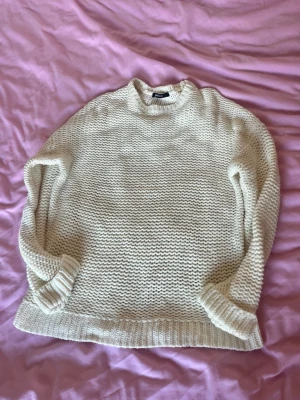 Krämvit stickad tröja - Mysig krämvit stickad tröja från Gina tricot med grovstickad struktur. Tröjan har rund halsringning, långa ärmar och ribbade muddar vid ärmslut och nederkant. Perfekt för lager på lager och enkel att matcha med jeans eller kjol.