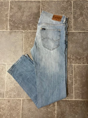 Ljusblå raka jeans från Lee - Säljer ett par ljusblå jeans från Lee med klassisk femficksmodell och raka ben. Jeansen har en snygg tvättad look och Lee-lapp bak i midjan. Tillverkade i bomull för en skön och avslappnad känsla.