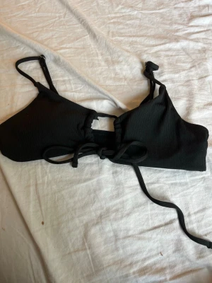 Svart ribbad bikiniöverdel med knyt - Snygg svart bikiniöverdel från SHEIN i ribbat material. Modellen har smala axelband och knytning framtill för en justerbar passform. Perfekt för strand eller poolhäng i sommar!