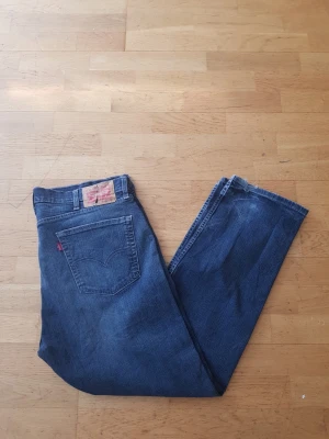 Levi's 505 - Klassiska blå jeans från Levi's med rak passform och femficksdesign. Jeansen har en tydlig läderpatch bak i midjan och den ikoniska röda Levi's-taggen på bakfickan. Tillverkade i slitstark denim, perfekta för en avslappnad och tidlös stil.