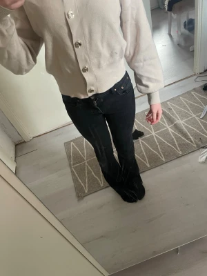 Beige kofta med stora knappar - Snygg beige kofta med stora, glansiga knappar framtill. Koftan har lång ärm, ribbade muddar och en rak, något kortare passform. Perfekt att slänga över en t-shirt eller linne för en chill look.