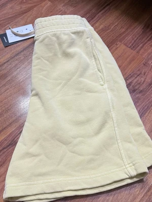 Gula shorts med resår och snörning - Snygga ljusgula shorts med elastisk midja och snörning. Modellen är loose fit och har praktiska sidofickor. Perfekta för varma dagar och chill stunder. Materialet är mjukt och bekvämt, troligtvis bomull.