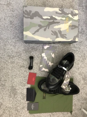 Valentino Rockrunners - Snygga sneakers från Valentino med camo-mönster i grönt, svart och grått. Skorna har svarta snören, detaljer i mocka och läder samt en robust sula. Perfekta för dig som vill sticka ut med en exklusiv streetstyle-look. (Rep)