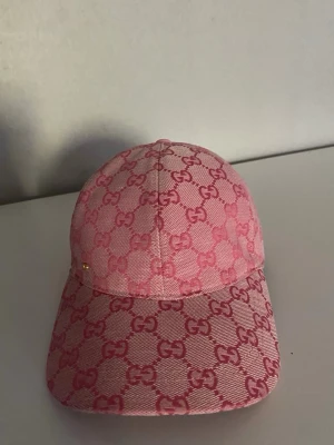 Rosa keps med GG-mönster - Säljer en snygg rosa keps  med klassiskt GG-monogram i hela tyget. Kepsen har böjd skärm och är tillverkad i ett slitstarkt tygmaterial. Perfekt accessoar för att lyfta din outfit med en lyxig touch.