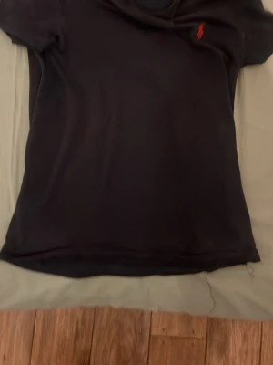 Svart slim fit t-shirt från Polo Ralph Lauren - Snygg svart t-shirt från Polo Ralph Lauren i slim fit-modell. Klassisk design med korta ärmar och den ikoniska röda loggan broderad på bröstet. Perfekt basplagg som funkar till allt och är tillverkad i mjuk bomull. Har solbleknad på ryggen.