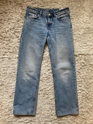 Blå Weekday Arrow jeans - Säljer ett par klassiska blå jeans med rak passform och snygg vintage-tvätt. Jeansen har fem fickor, bälteshällor och knappgylf. Det har dock gått sönder vid fickan men går lätt att sy upp